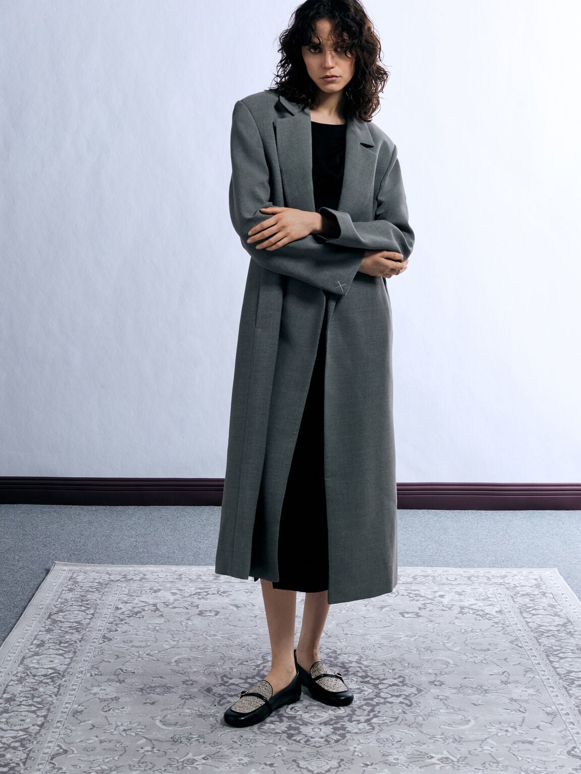 A long-tailored coat paired with black maxi dress, with parts of the black dress peeking through. 