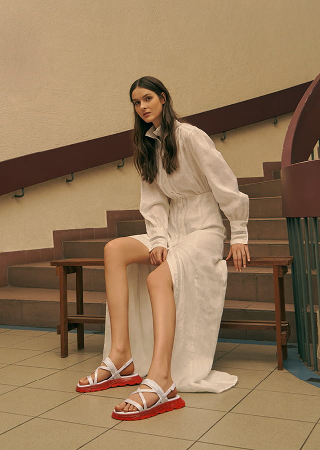 A model wearing a white maxi dress with strappy flatform sandals.