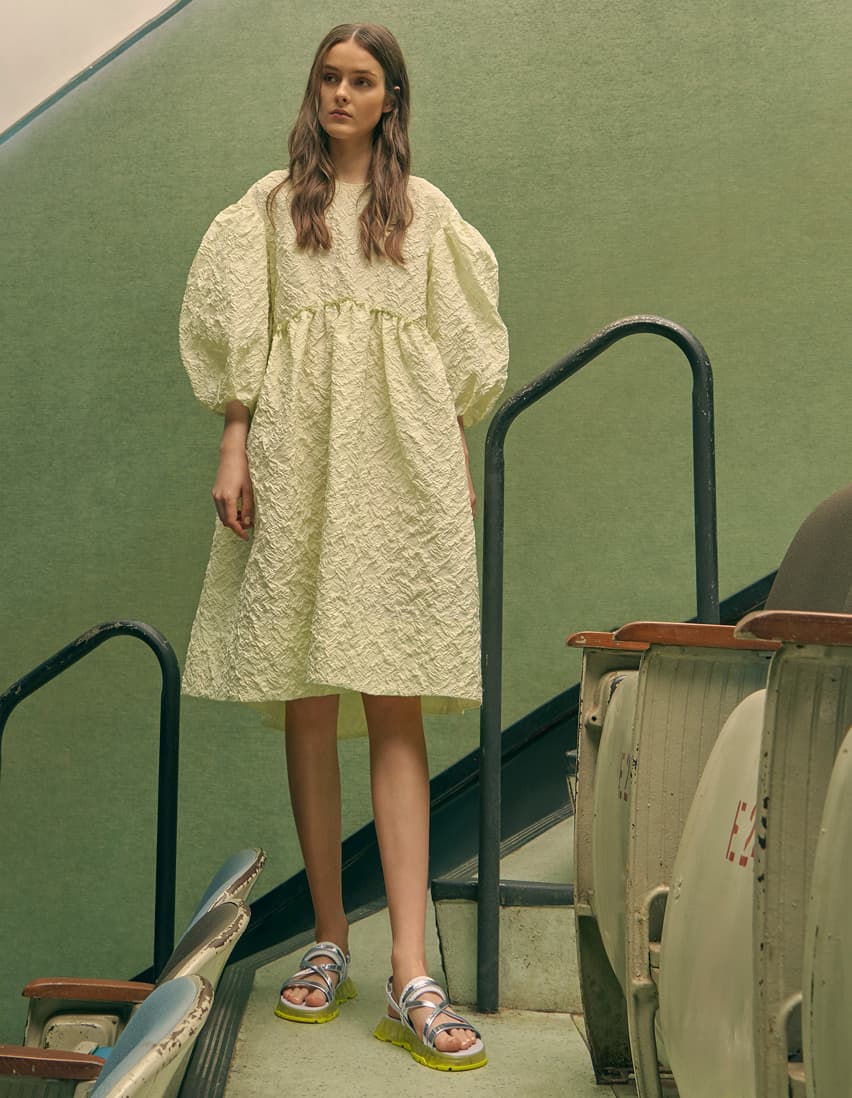 A model wearing a puff sleeve babydoll dress with metallic strappy flatform sandals.