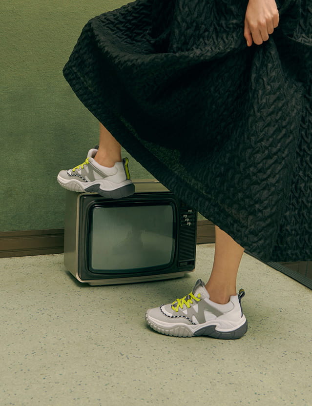 A collage of a model in mesh chunky sneakers, a metallic top handle box bag and metal frame sunglasses.