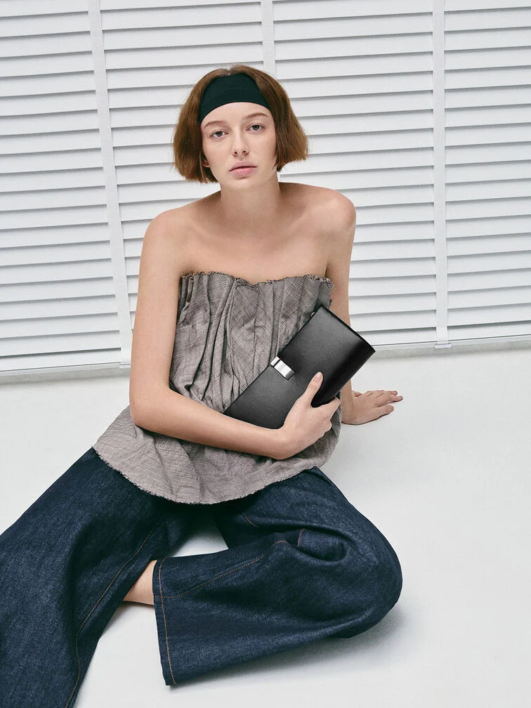 Clutch held securely from the bottom with the thumb over the front and fingers underneath, illustrating a practical and poised grip.