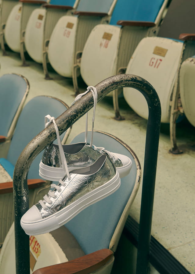 Shiny metallic platform sneakers hanging from a metal bar by their laces.