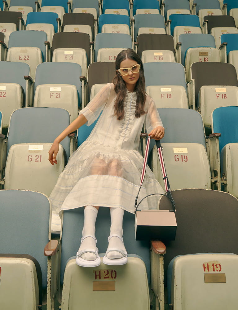 A model in velcro strap sandals, a top handle box bag and printed geometric frame sunglasses.