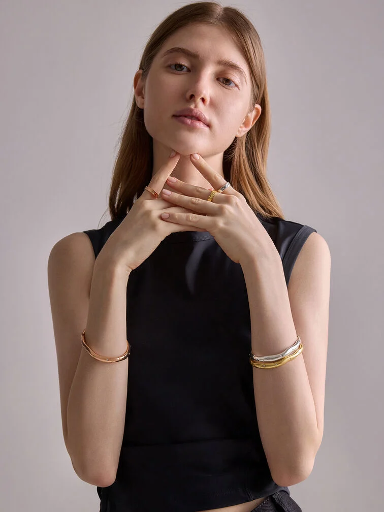 A mixed-metal bracelet stack, featuring a silver and yellow-gold sculptural bangle on one hand, and a single rose-gold bangle on the other.