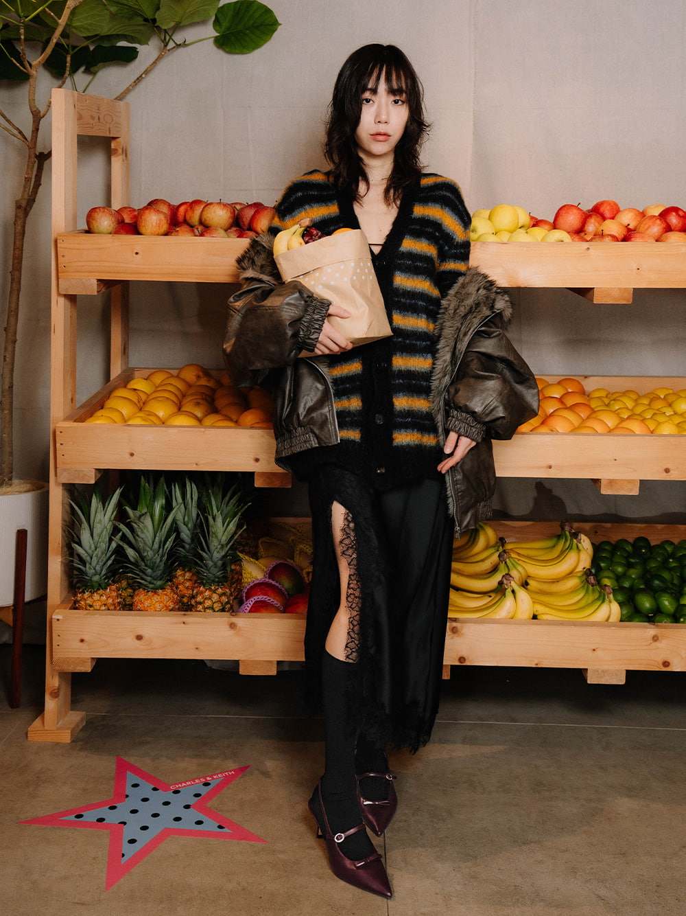 Shot of KOL posing with our fruit-wall display wearing the Sonali bow slingback pumps in burgundy - CHARLES & KEITH