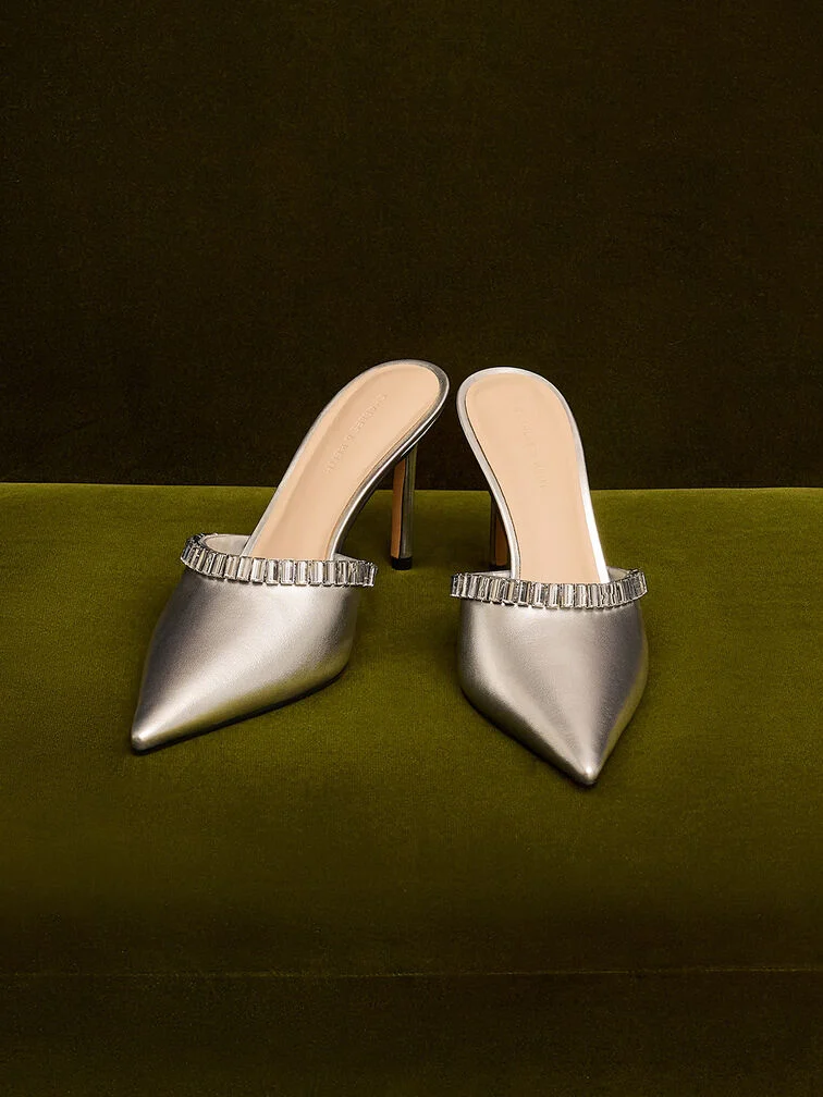 Metallic silver pointed-toe heeled mules adorned with crystal embellishments.