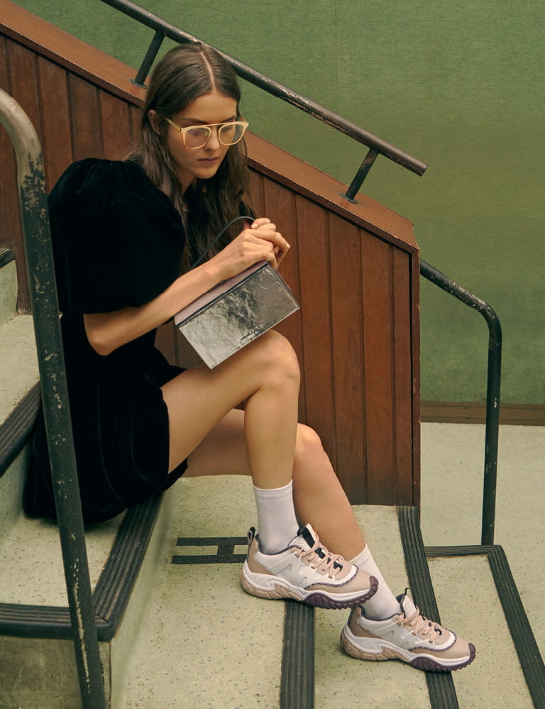A collage of a model in mesh chunky sneakers, a metallic top handle box bag and metal frame sunglasses.